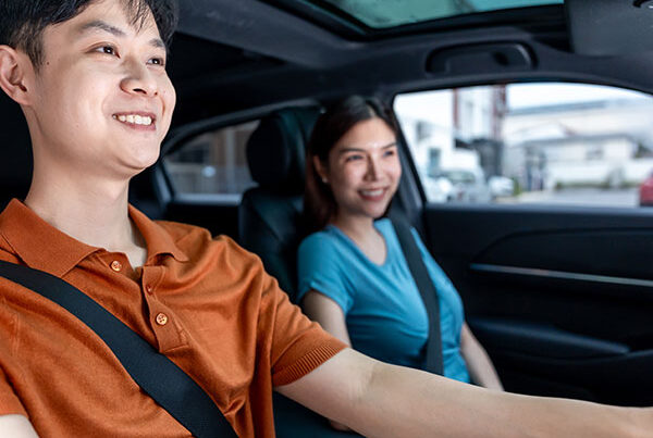 Asian woman supervising a male learner driver at the wheel of a car.